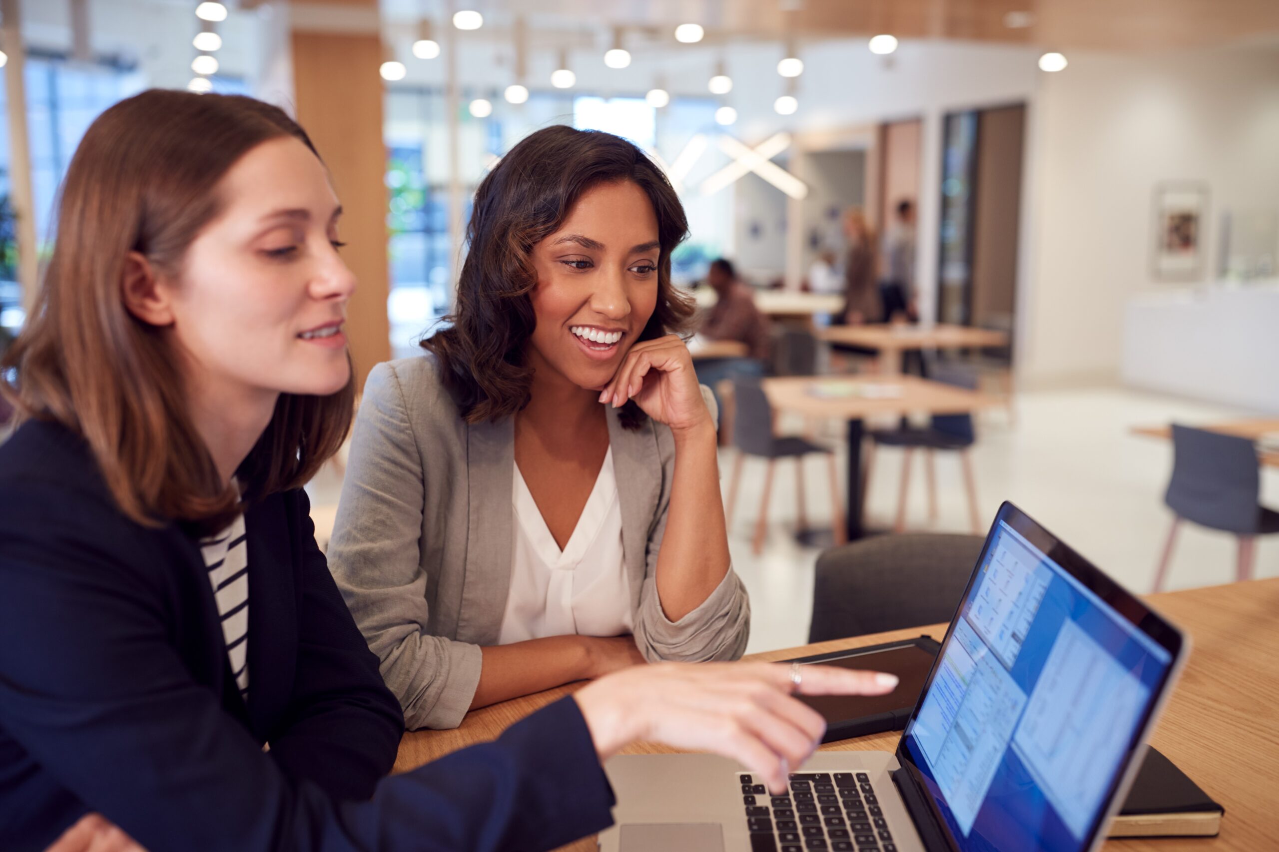 Two Businesswomen With Laptop At Desk In Open Plan Office Collaborating On Project Together